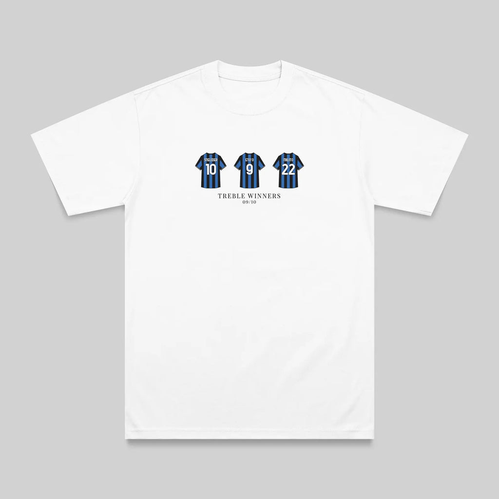 A white short-sleeve crewneck t-shirt with a graphic on the chest showing three blue and black striped jerseys with the number 15, and the text 'TREBLE WINNERS' underneath, displayed on a neutral gray background.