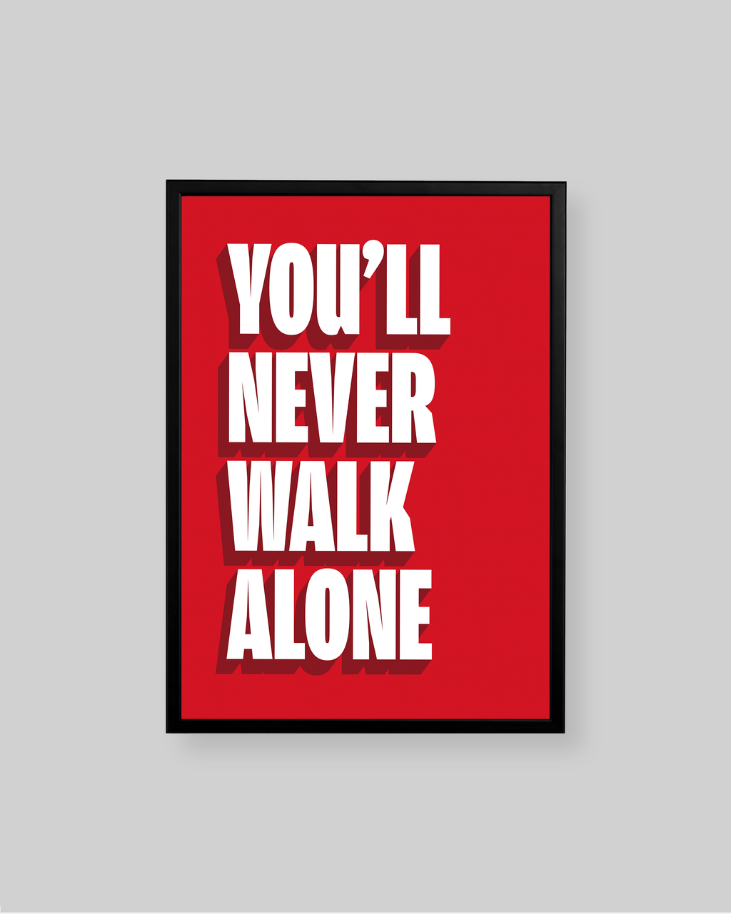 A framed motivational poster with the text 'YOU'LL NEVER WALK ALONE' in bold white letters on a bright red background, shown against a light gray wall.