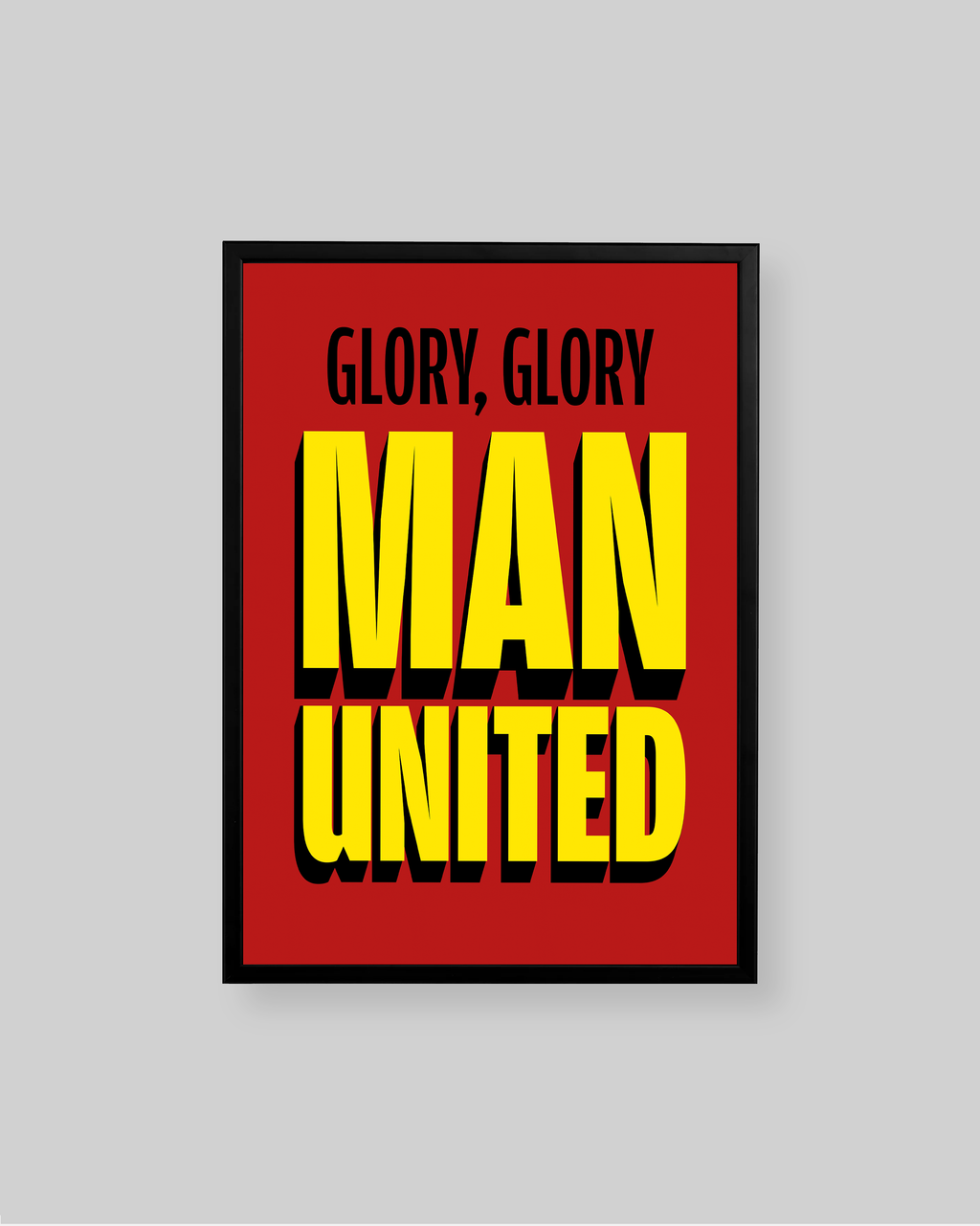 A framed poster with a bold red background and large yellow text reading 'MAN UNITED' with smaller black text above reading 'GLORY, GLORY'. The poster is shown against a light gray background.