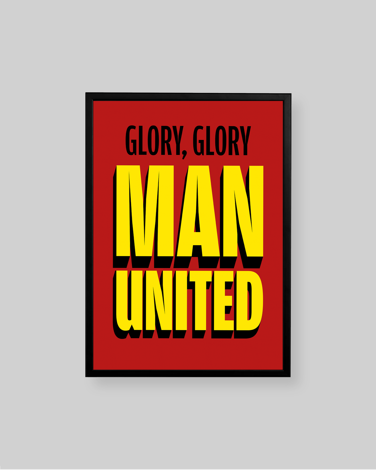 A framed poster with a bold red background and large yellow text reading 'MAN UNITED' with smaller black text above reading 'GLORY, GLORY'. The poster is shown against a light gray background.