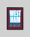 A framed typographic wall art print with the words 'WEST HAM ARE MASSIVE' in bold white and light blue lettering on a dark red background, shown against a light gray wall.