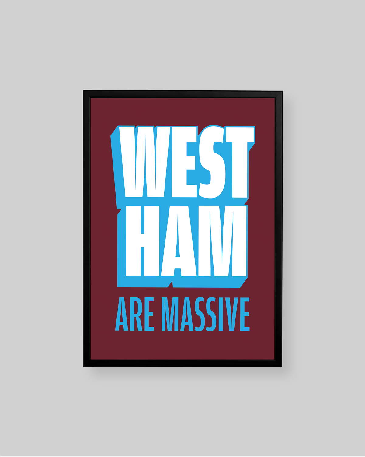 A framed typographic wall art print with the words 'WEST HAM ARE MASSIVE' in bold white and light blue lettering on a dark red background, shown against a light gray wall.